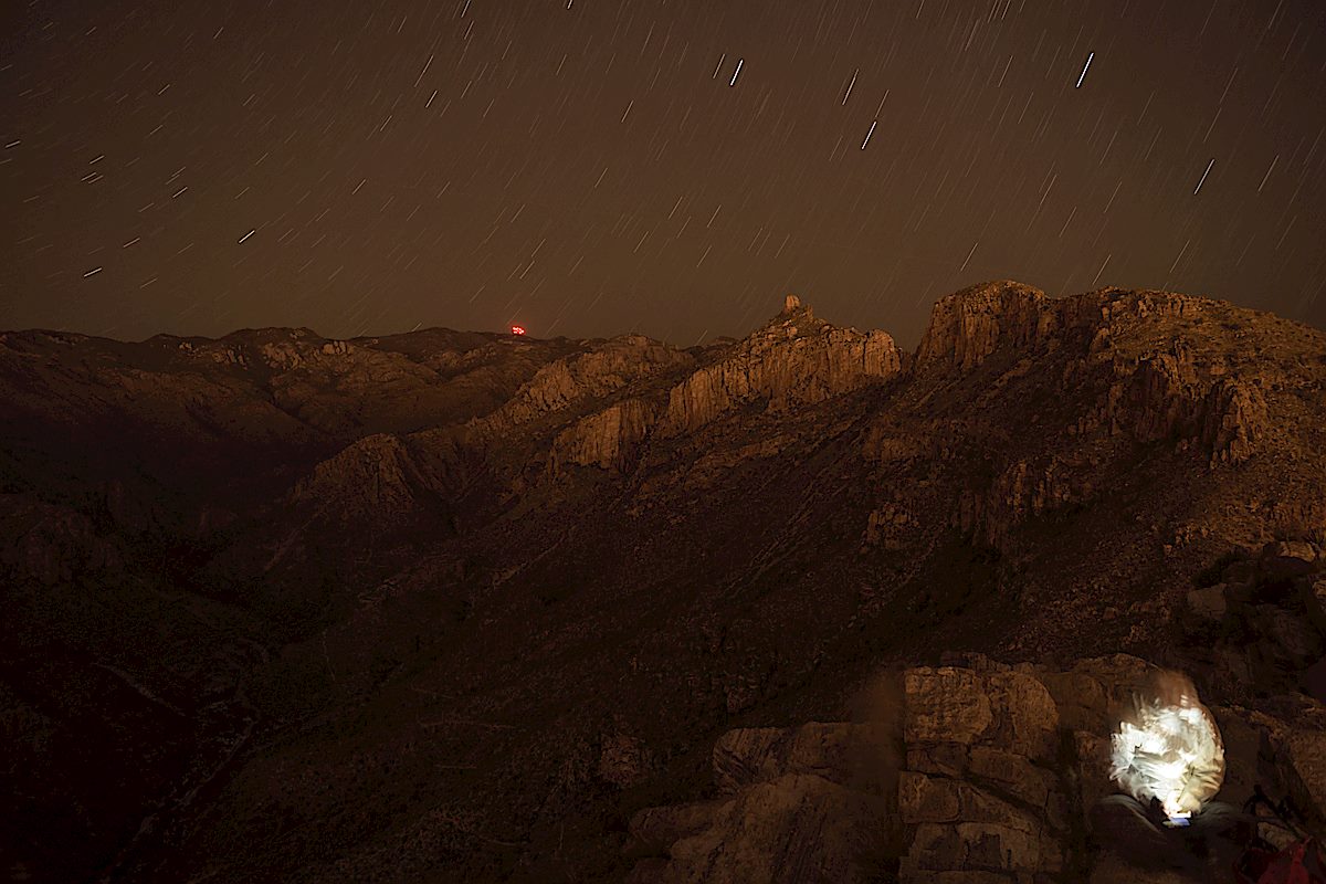 Taking a break at the top of Blackett's Ridge on a night hike - city and starlight illuminating the mountains, the red lights of Mount Bigelow in the background. September 2013